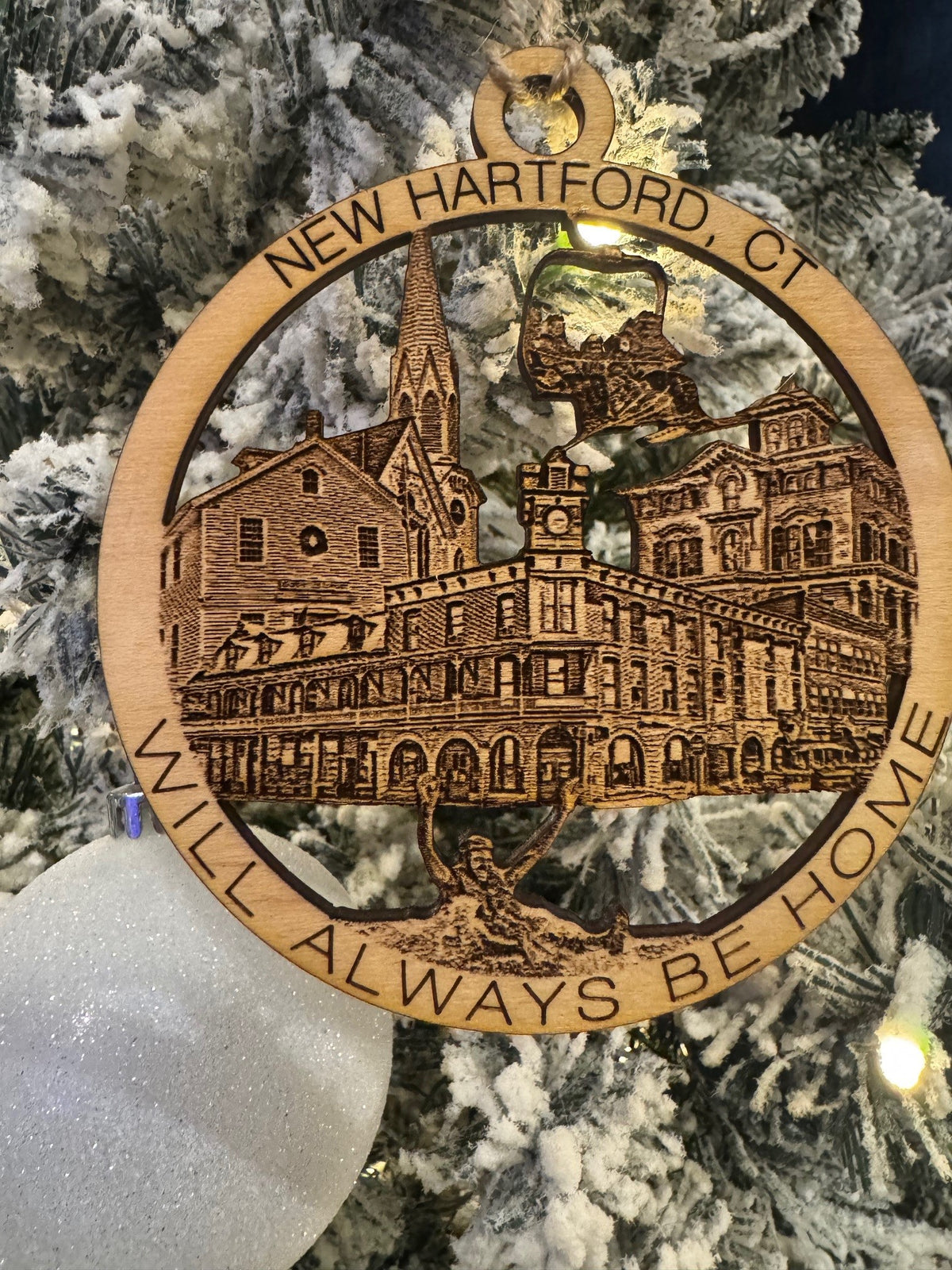 A wooden ornament with an engraved image of New Hartford, CT landmarks and the text 'NEW HARTFORD, CT ALWAYS HOME'.